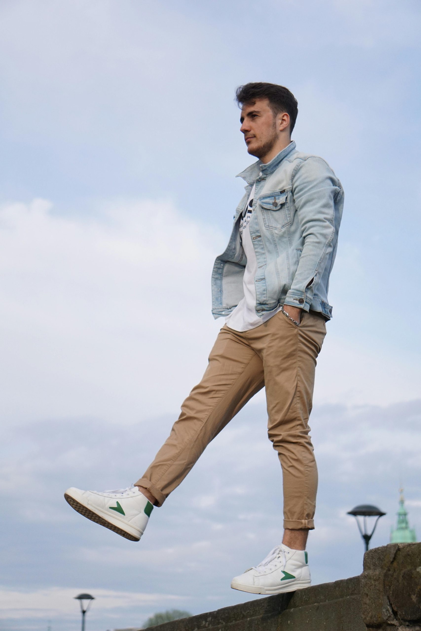 Jeune homme en veste en jean et baskets blanches debout en extérieur à Cracovie