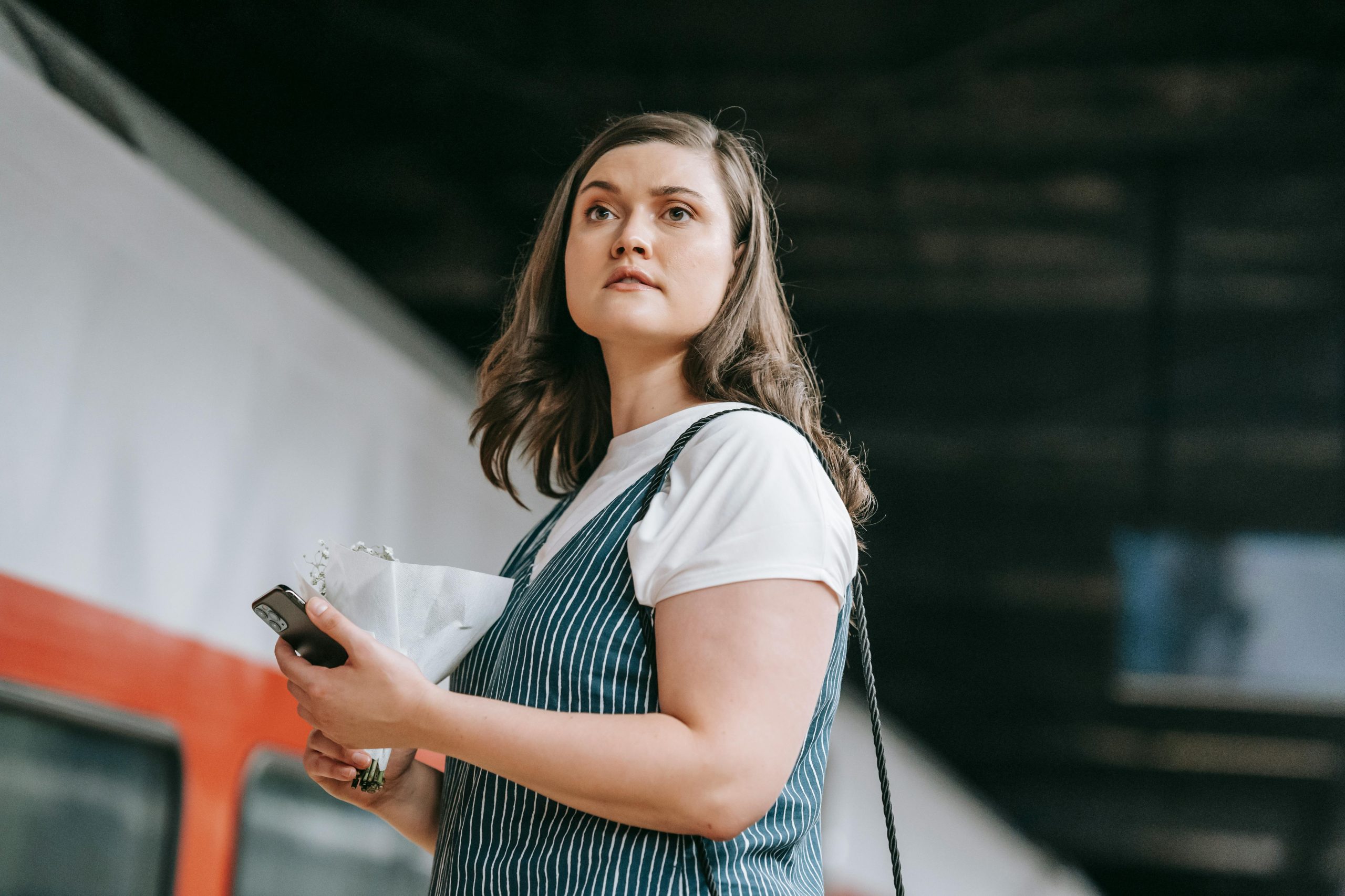 Jeune femme utilisant son téléphone dans une gare, attendant le départ sous un éclairage tamisé