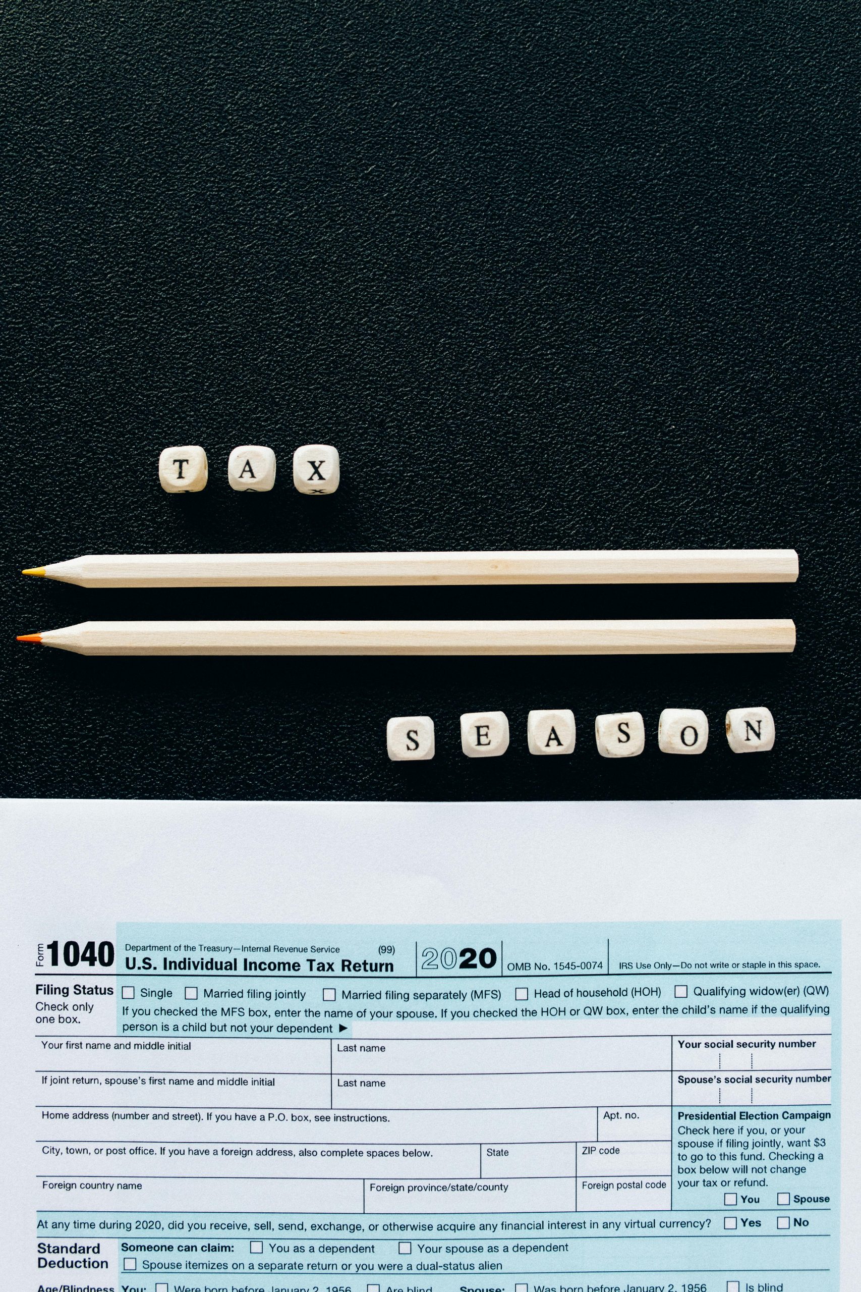 Créative composition mettant en scène un formulaire d'impôt 1040, des crayons et des lettres formant "Tax Season" sur fond noir.