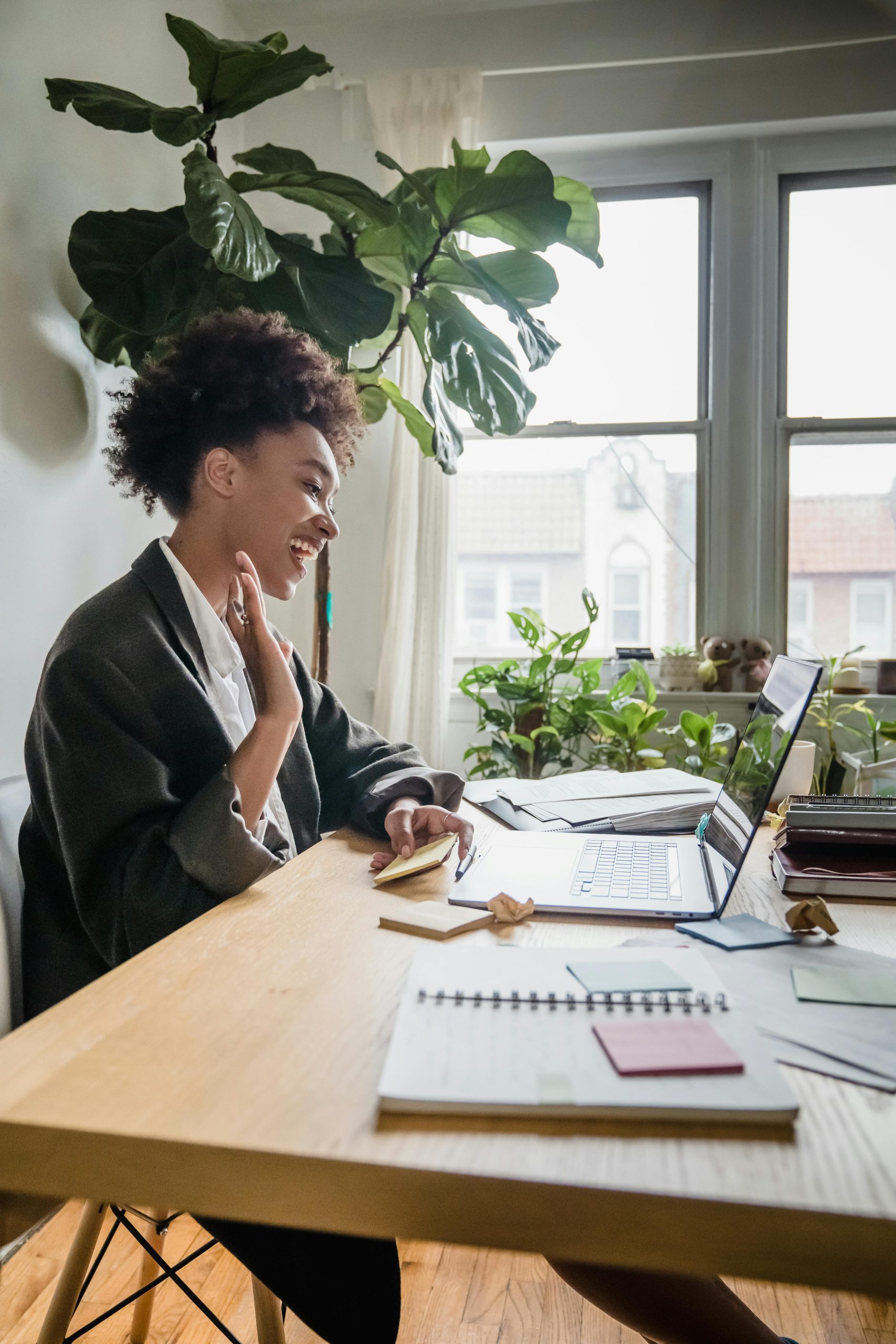 Femme souriante en visioconférence au bureau à domicile, engageante et faisant un signe de la main à son écran d'ordinateur portable.