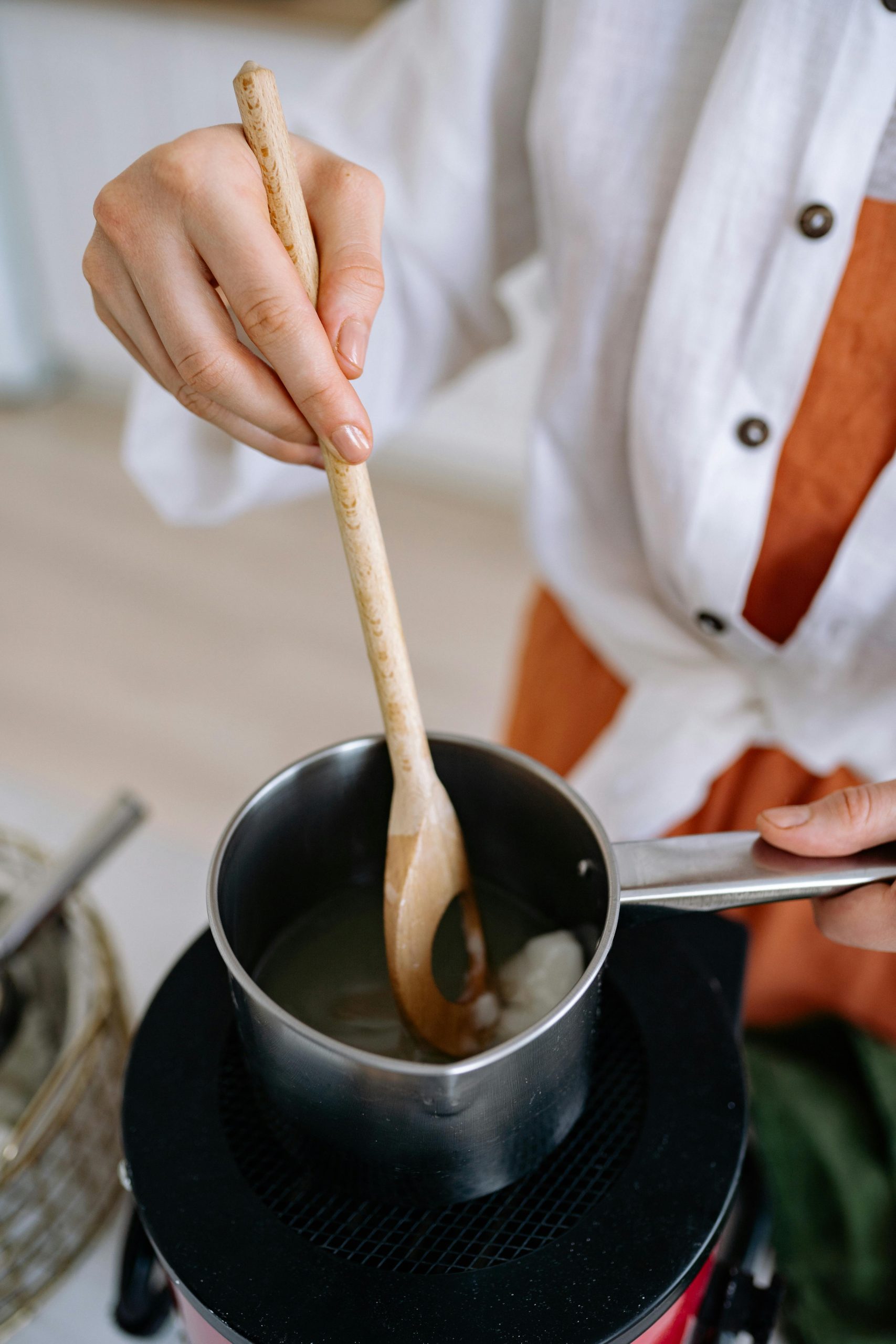 Proche plan de mains remuant de la cire dans une casserole, illustrant la fabrication de bougies DIY.
