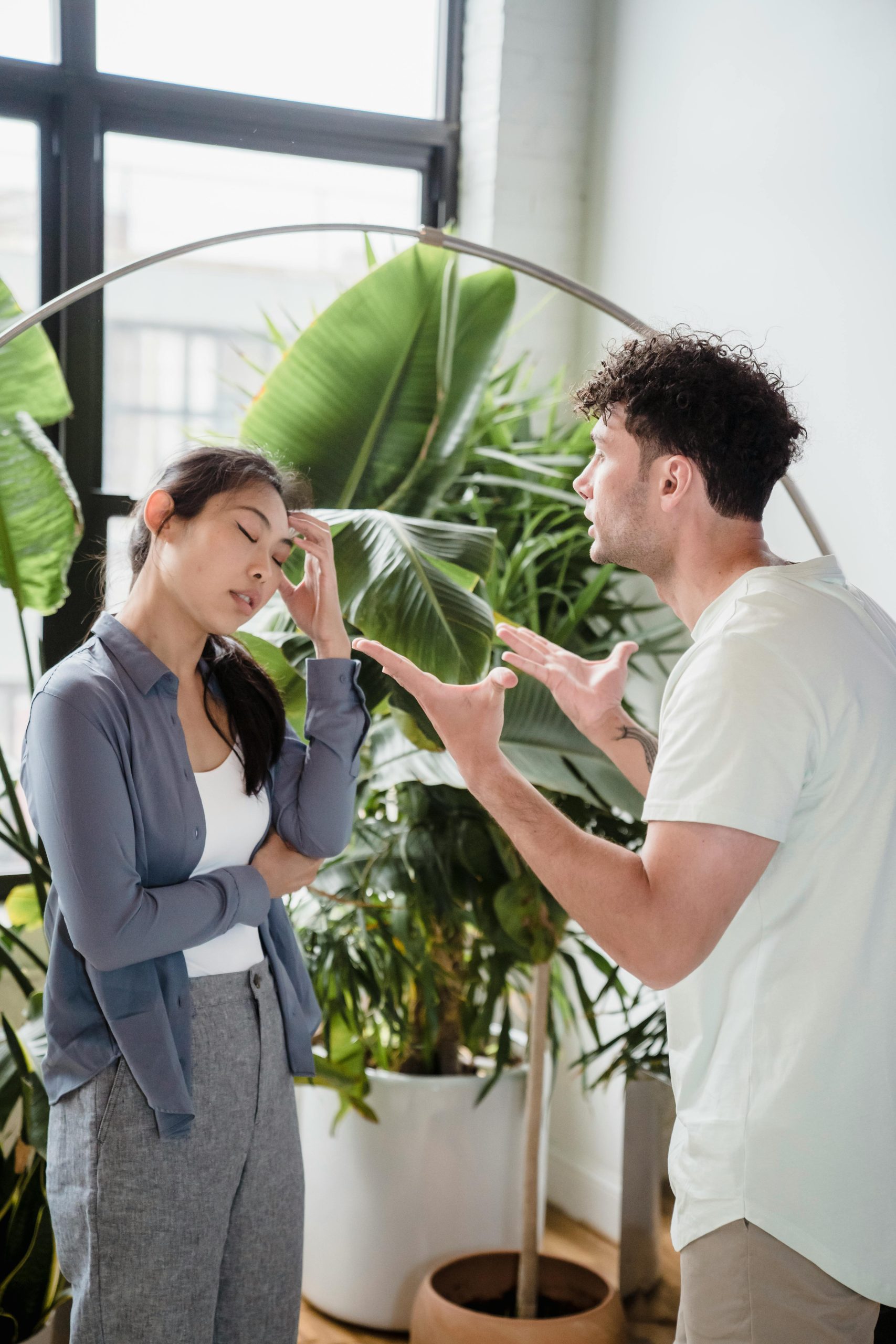 Un homme et une femme en pleine dispute animée à l'intérieur, entourés de plantes.