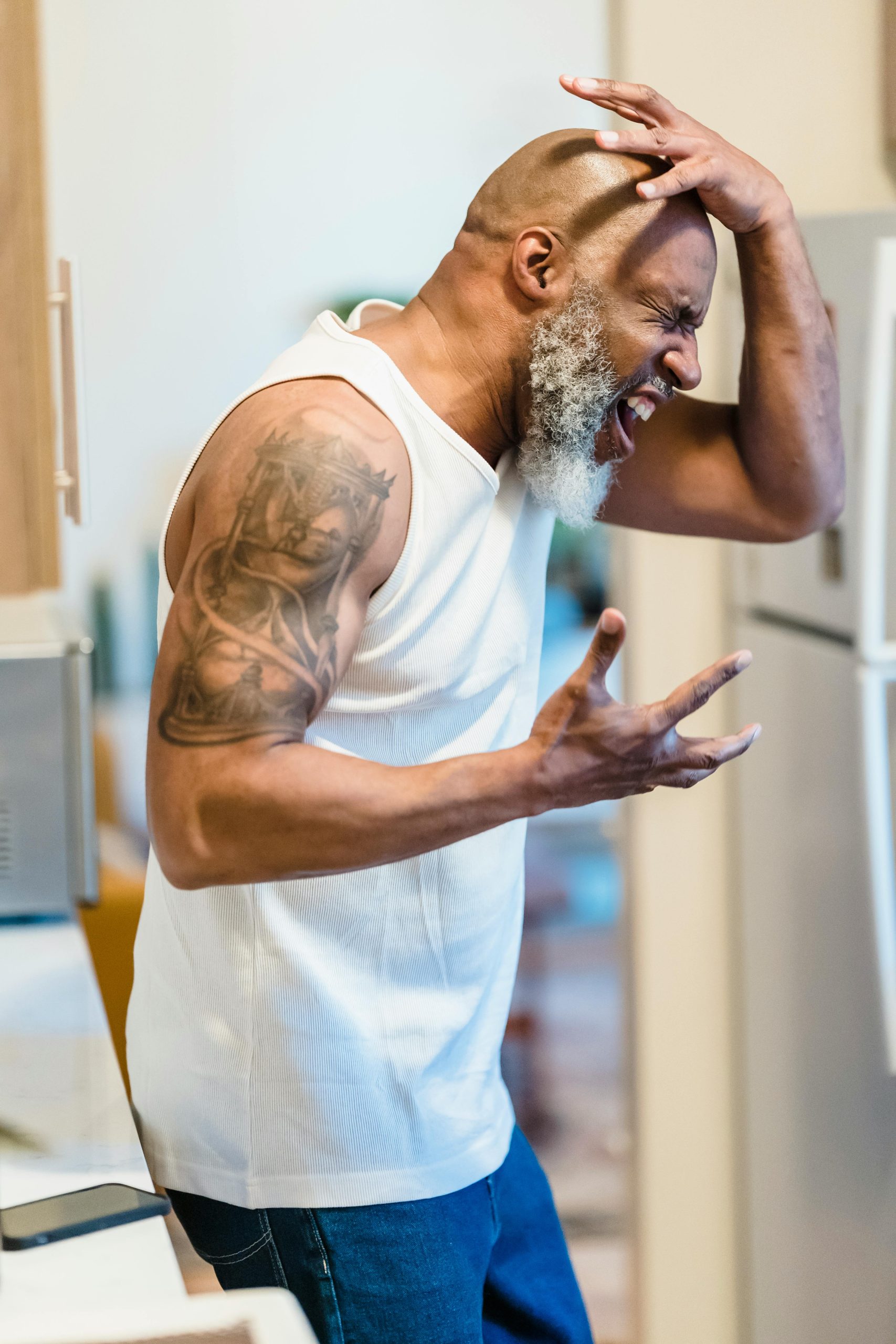 Homme afro-américain chauve et barbu criant avec colère dans une cuisine.