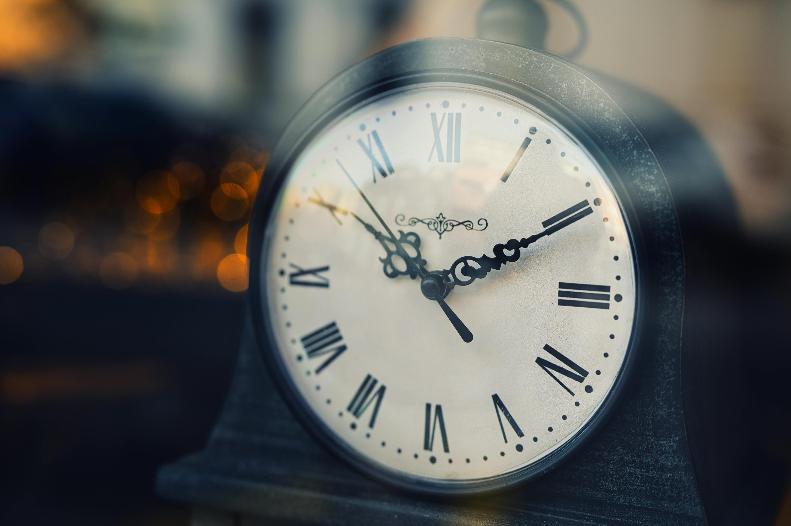 Close-up of a vintage clock with Roman numerals, softly lit background. Gros plan d'une horloge vintage avec des chiffres romains, arrière-plan doucement éclairé.