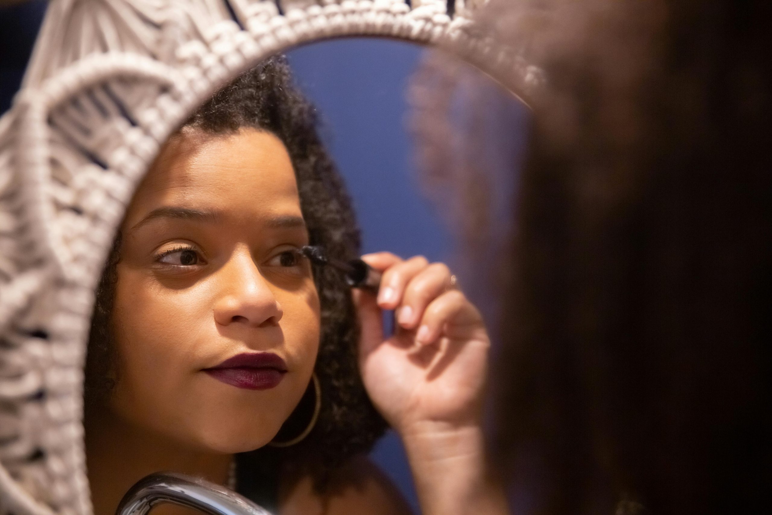 Close-up of a woman applying mascara in a mirror reflection, emphasizing beauty and care. Gros plan d'une femme appliquant du mascara dans le reflet d'un miroir, mettant l'accent sur la beauté et les soins.
