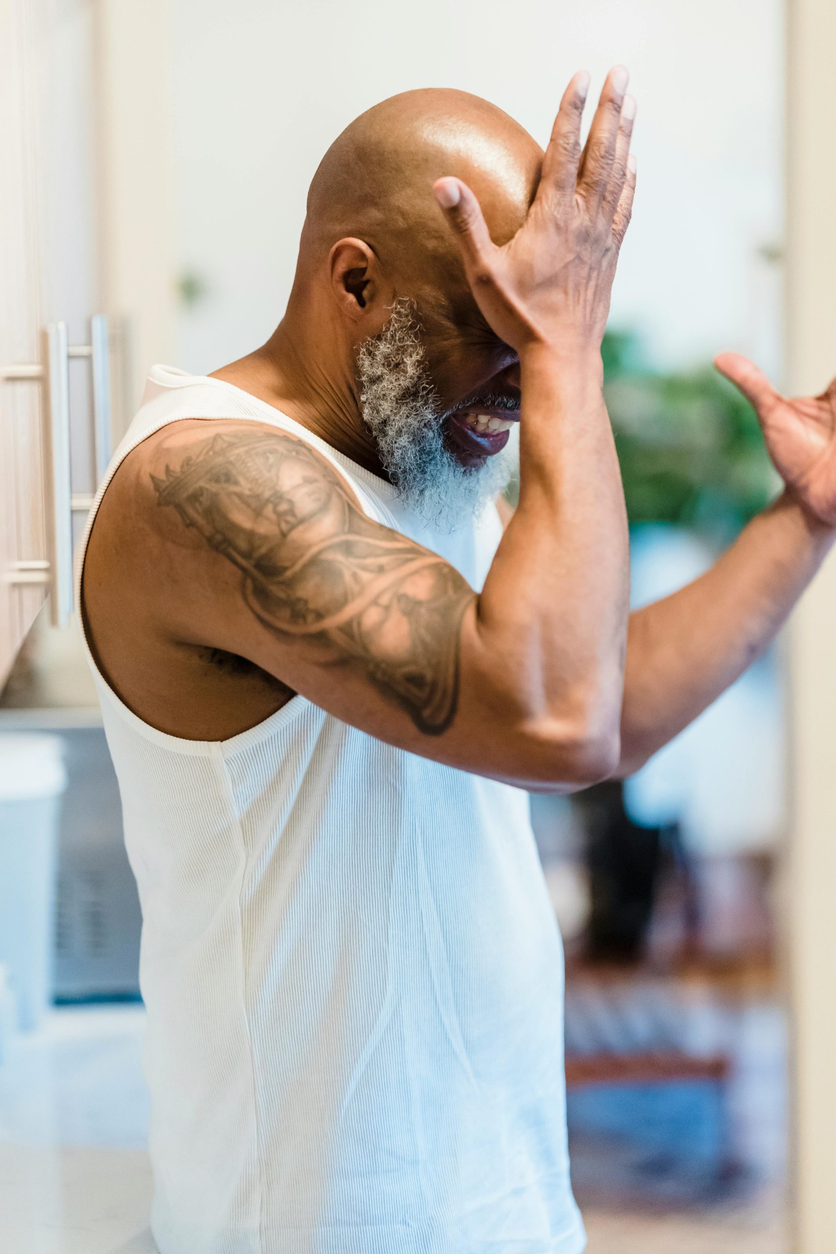 An adult man with a tattoo expresses stress and regret in an indoor setting. Un homme adulte avec un tatouage exprime le stress et le regret dans un cadre intérieur.