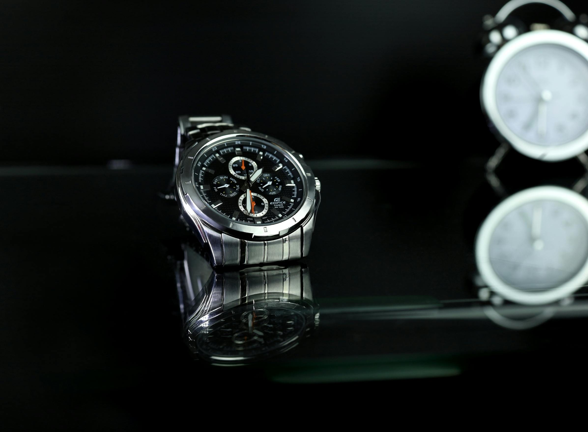 Stylish silver wristwatch with black dial in a fashion photography setting on reflective glass. Montre-bracelet argentée élégante avec cadran noir dans un décor de photographie de mode sur verre réfléchissant.