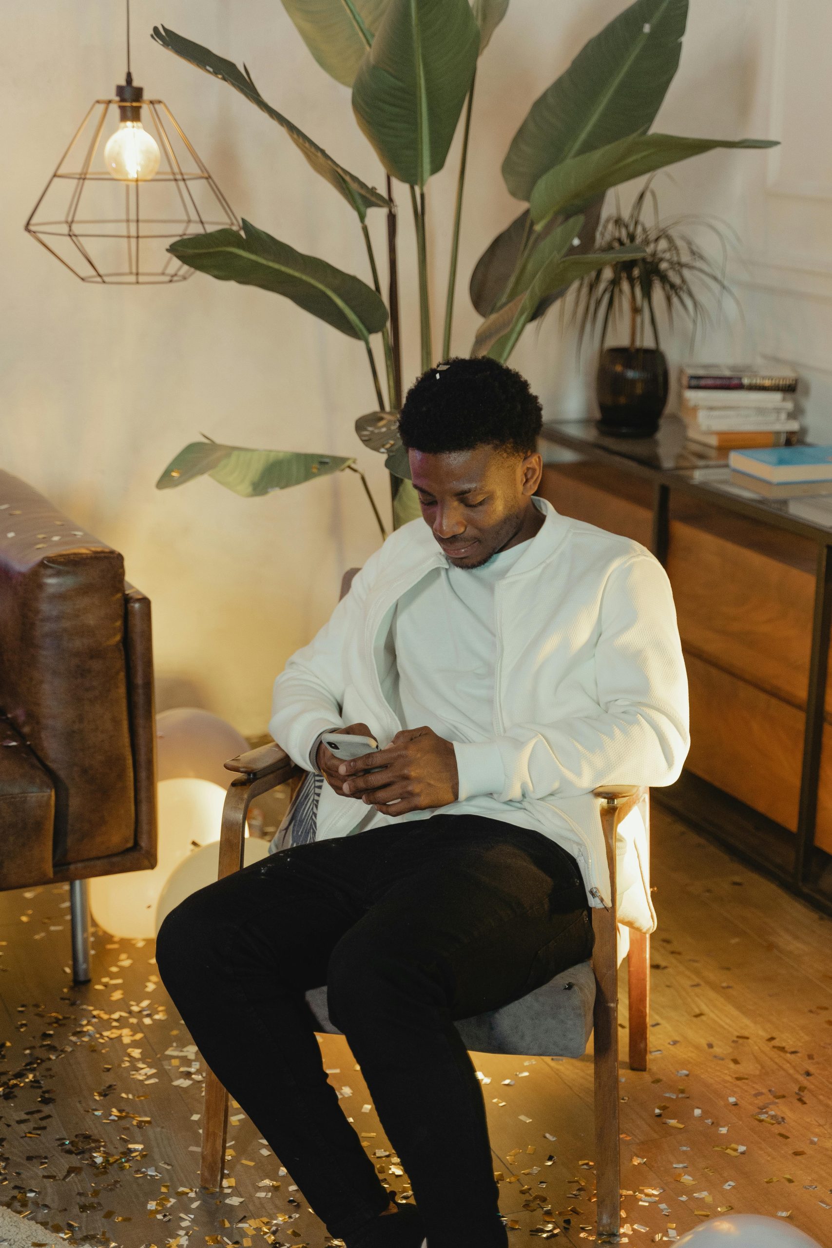 Homme vêtu de manière décontractée assis sur une chaise utilisant un smartphone dans un cadre de pièce confortable.