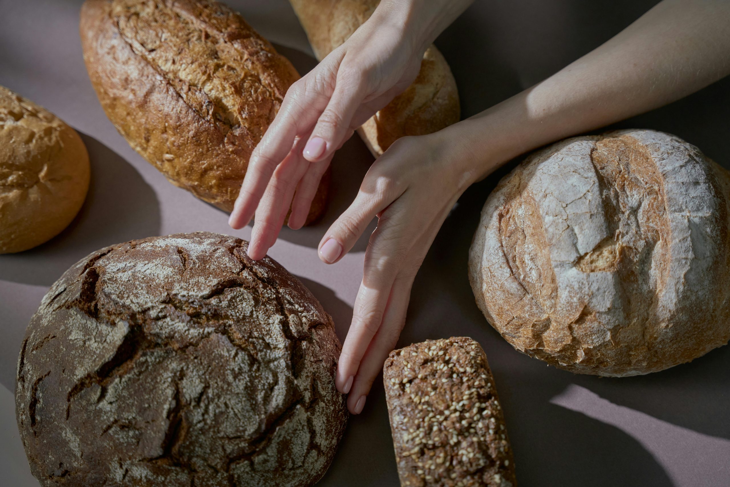 Hands gently touching various homemade breads in a warm-lit, artistic food photography shot. Des mains touchant délicatement différents pains faits maison dans une photographie culinaire artistique avec un éclairage chaleureux.