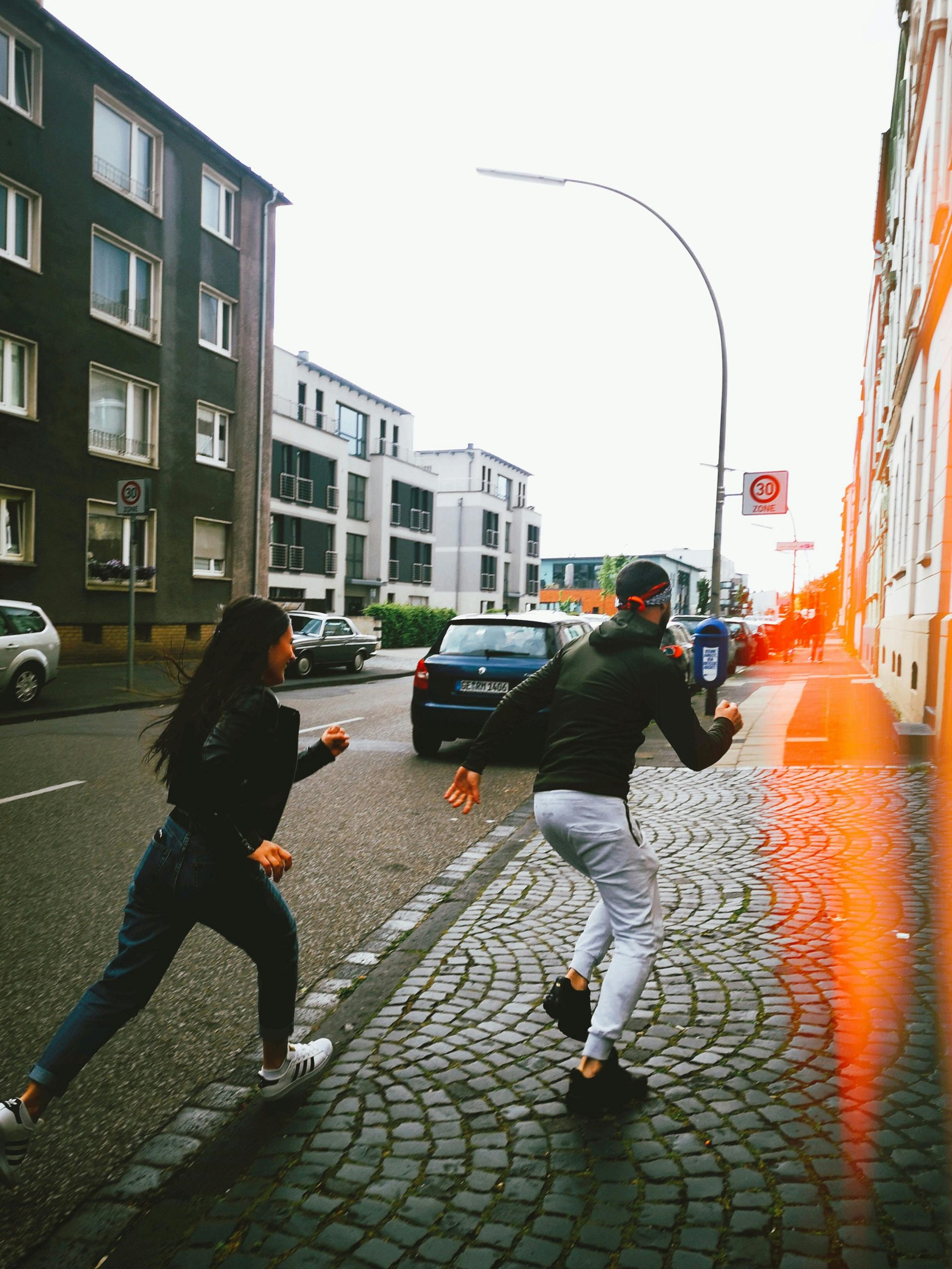 Dynamic urban street scene with two people running on a cobblestone sidewalk. Scène urbaine dynamique avec deux personnes courant sur un trottoir pavé.
