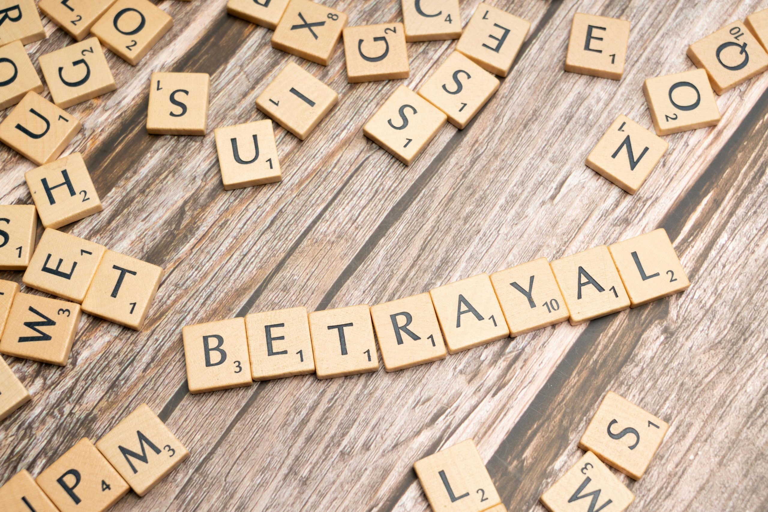 Wooden letter tiles spelling 'Betrayal' on a rustic wooden surface, conveying themes of deceit and dishonesty. Des tuiles en bois avec les lettres épelant « Trahison » sur une surface en bois rustique, évoquant des thèmes de tromperie et de malhonnêteté.