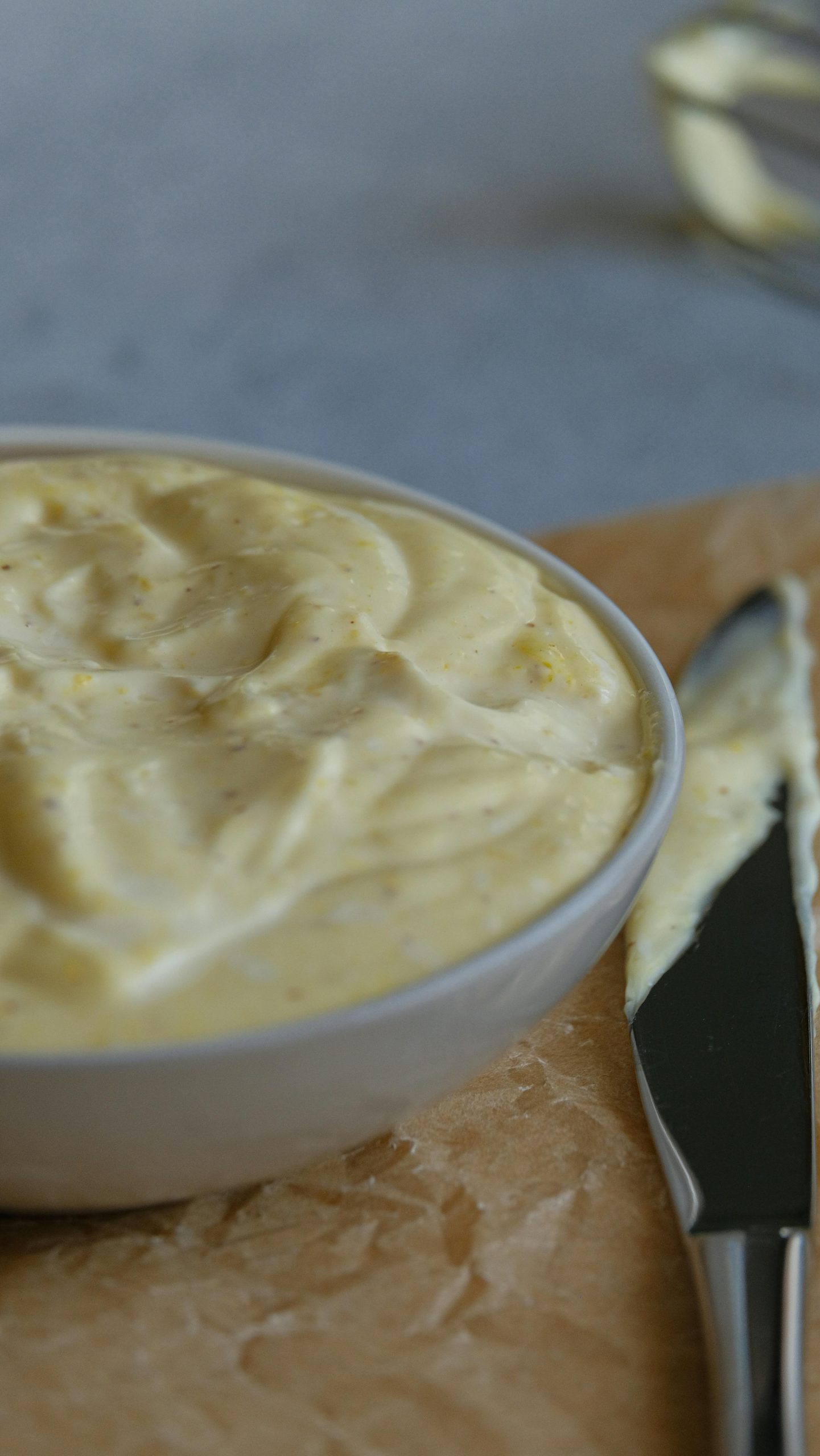 A bowl of creamy homemade mayonnaise on a cutting board with a spreading knife. Un bol de mayonnaise maison crémeuse sur une planche à découper avec un couteau à tartiner.