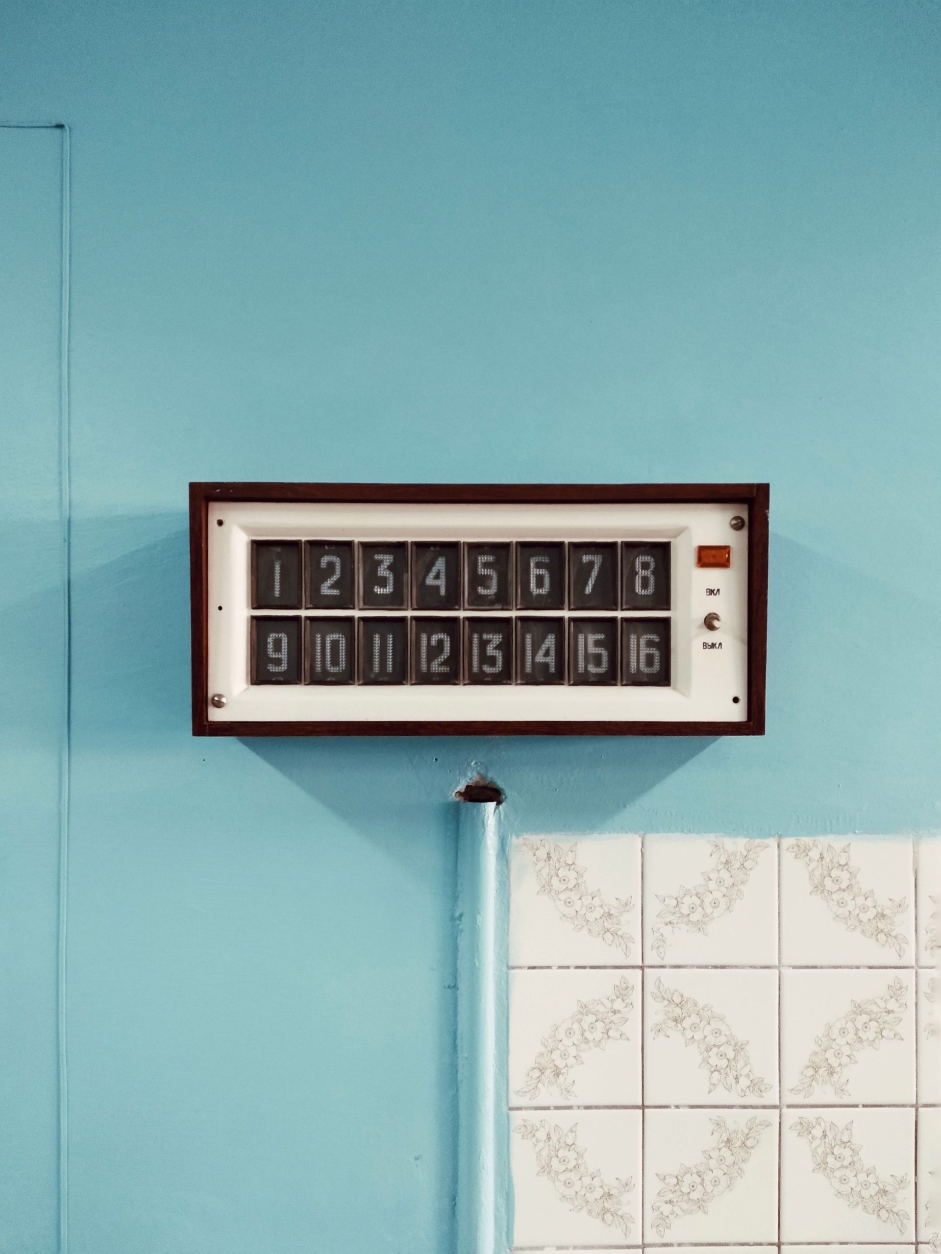 Retro wall clock displaying numbers on a blue tiled backdrop, perfect for decor inspiration. Horloge murale rétro affichant des chiffres sur un fond de carreaux bleus, parfaite pour l'inspiration décorative.