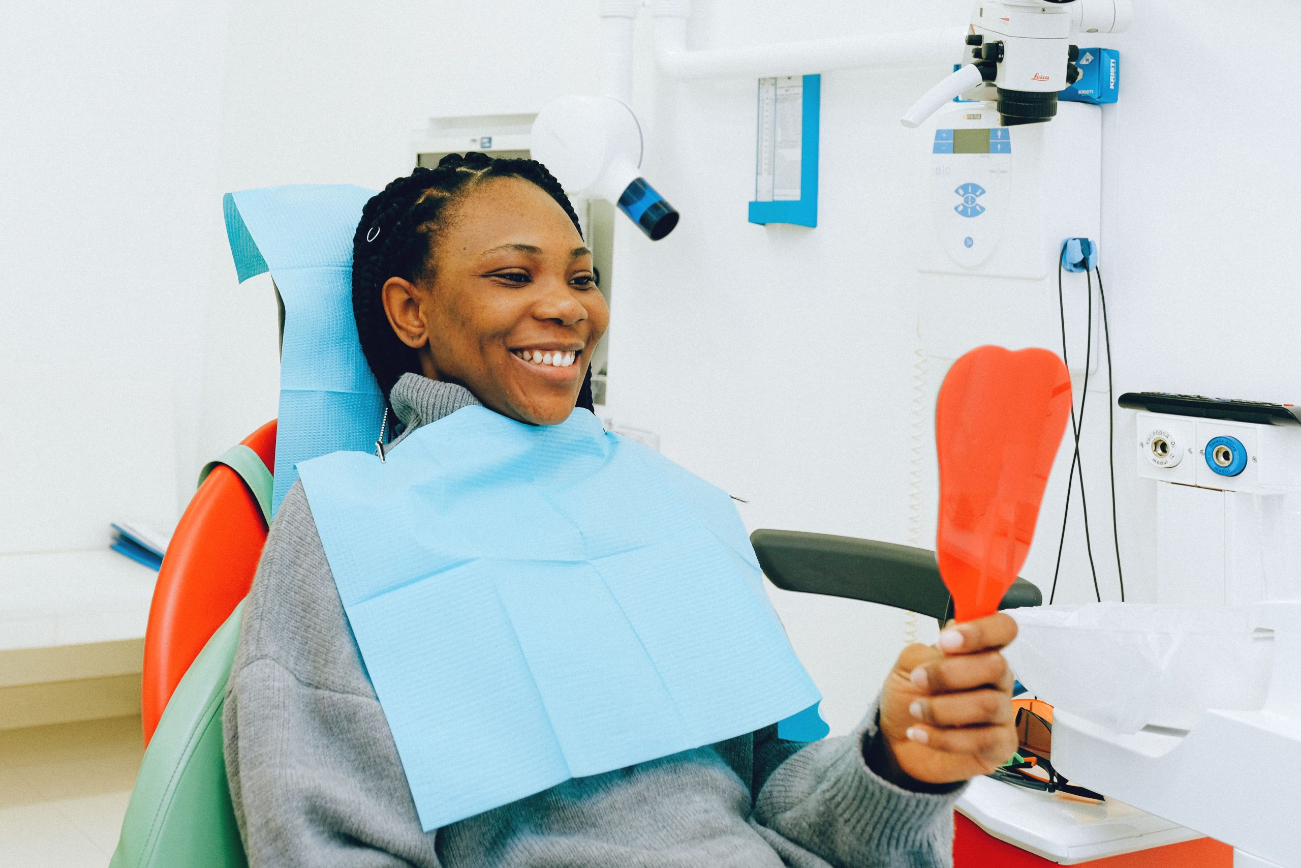 Femme souriante tenant un miroir lors d'un examen dentaire dans une clinique.