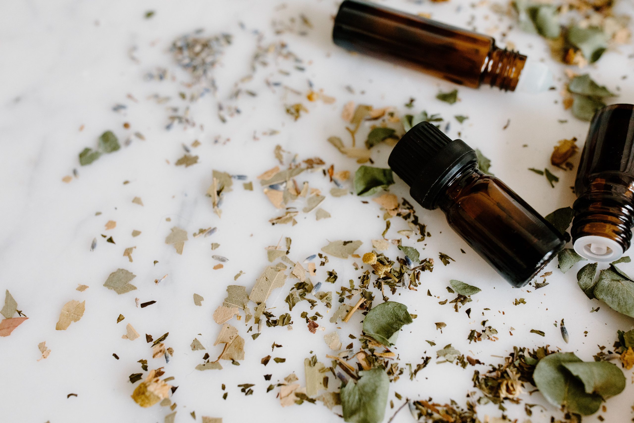 Aromatherapy setup with essential oil bottles and dried herbs on a white surface for holistic healing. Configuration d'aromathérapie avec des flacons d'huiles essentielles et des herbes séchées sur une surface blanche pour la guérison holistique.