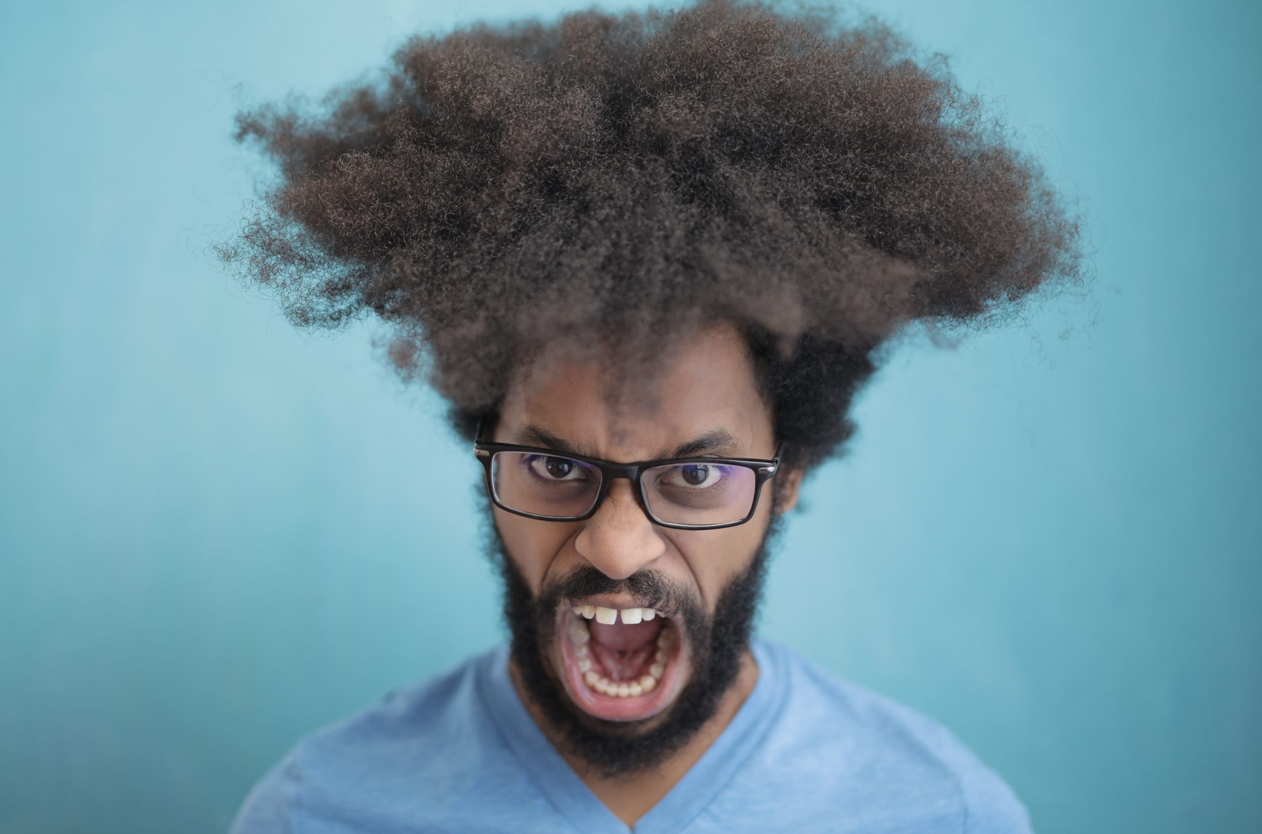 Portrait d'un homme aux cheveux afro portant des lunettes, exprimant une émotion sur un fond bleu.