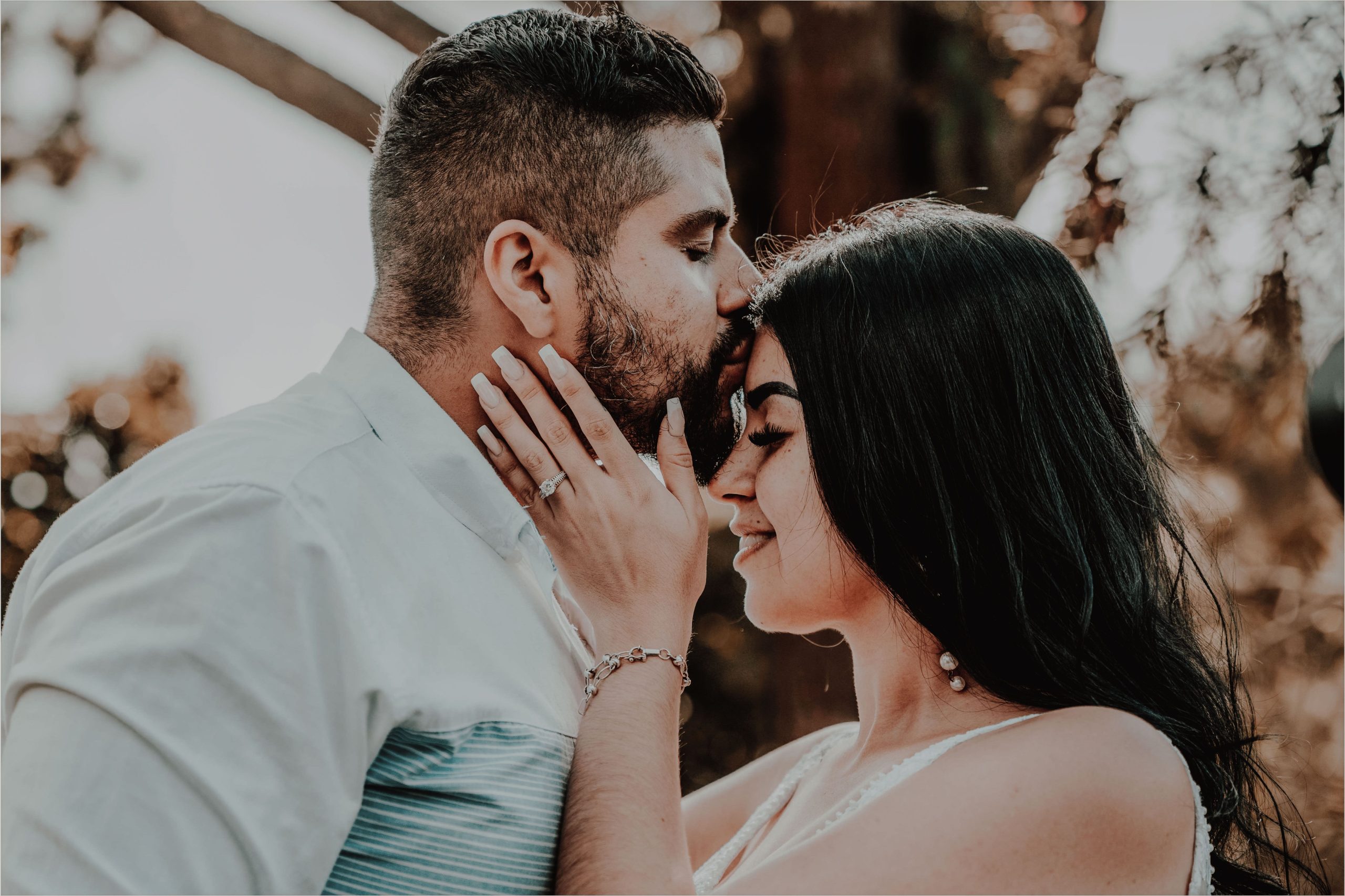 Tender moment of a couple sharing a forehead kiss outdoors, capturing love and serenity. Un moment tendre d'un couple partageant un baiser du front en plein air, capturant l'amour et la sérénité.