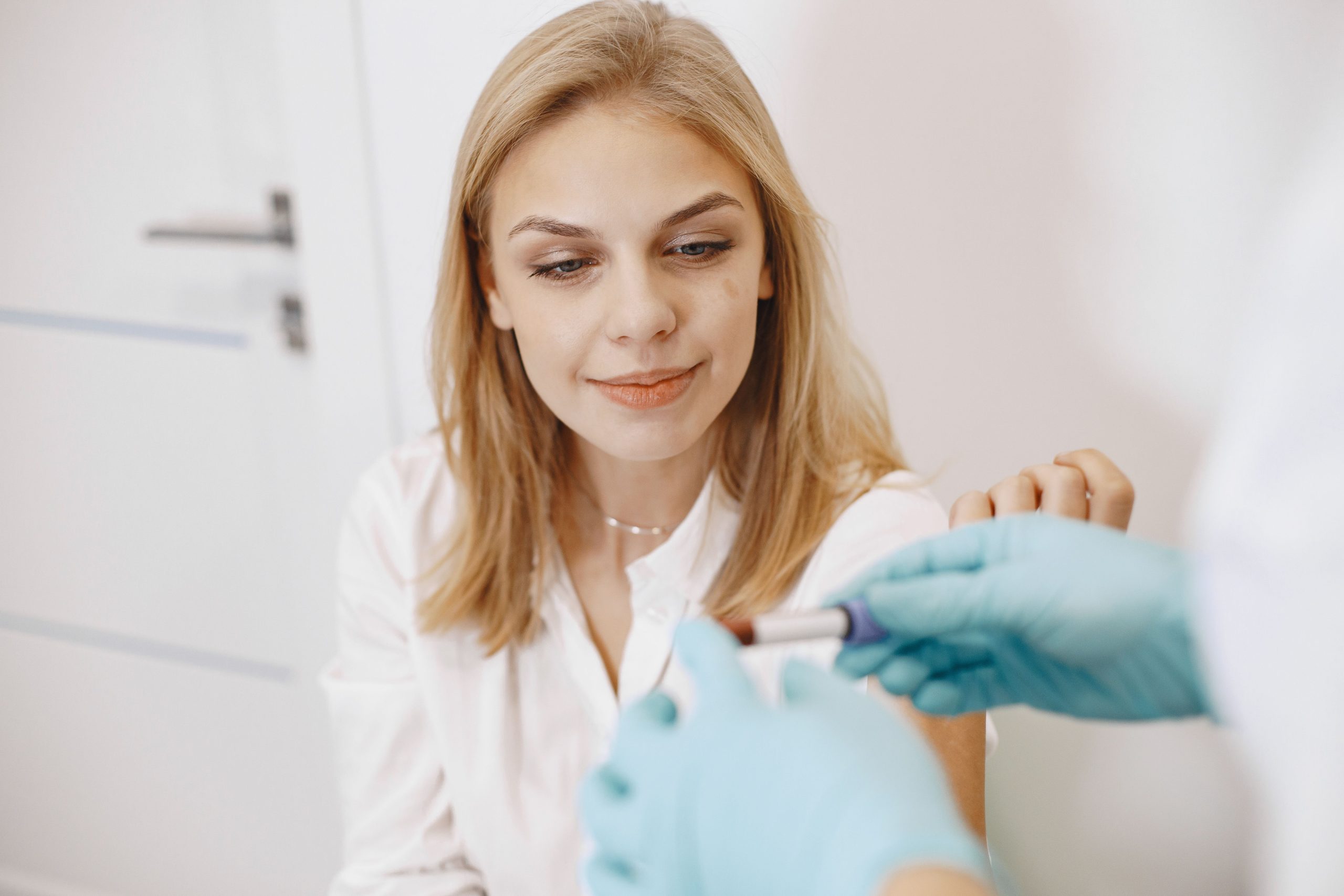 Blond woman in clinic receiving blood test with healthcare professional holding sample. Femme blonde dans une clinique recevant une prise de sang avec un professionnel de santé tenant l'échantillon.